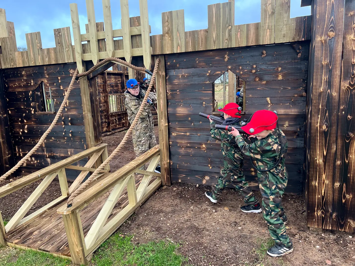 Children in red and blue laser tag caps playing beside the castle drawbridge at Escot Park